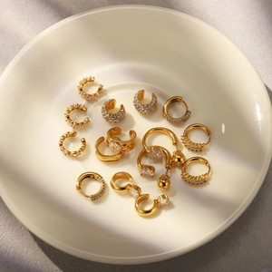 Detailed arrangement of gold-plated ear cuffs and zircon hoop earrings on ceramic tray