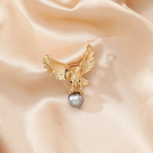 Broche aigle vintage dorée avec perle grise sur fond en satin couleur champagne