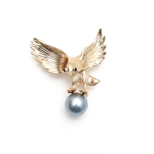 Vue détaillée d'une broche aigle dorée avec texture de plumes et grosse perle grise