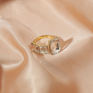 Golden geometric open ring with rectangular zircon stones on champagne silk fabric
