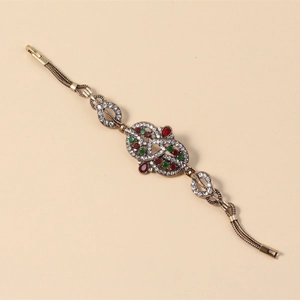 Detail eines Vintage-Boho-Armbands mit roten und grünen Steinen an einer Goldkette