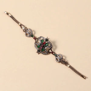 Detail eines Vintage-Goldarmbands mit roten und grünen Steinen und Metallgeflecht