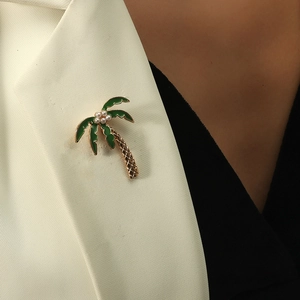 Broche palmier dorée avec émail vert et perles blanches sur un revers de blazer crème