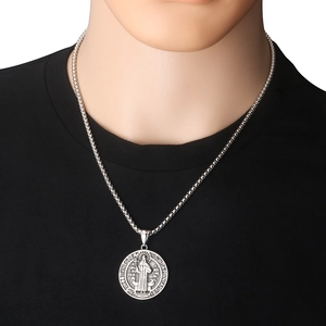 Primer plano del colgante medalla de San Benito en acero plateado sobre camiseta negra