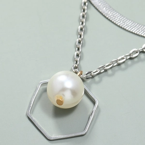 Detalle de collar multicapa con perla blanca y colgante geométrico de hexágono plata