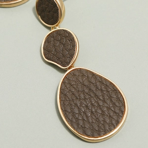 Macro detail of geometric long earrings with brown lychee leather and gold metal frames