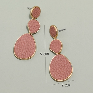 Detail view of drop earrings featuring gold metal frames with pink lychee leather texture