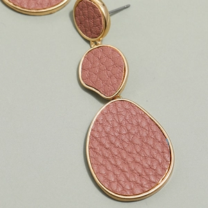 Macro detail of geometric drop earrings with gold metal and pink textured leather inlay