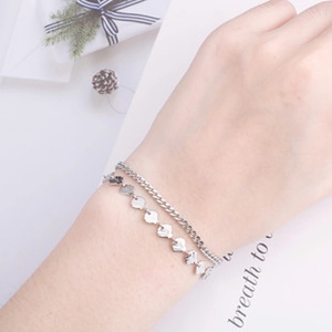 Dettaglio di un bracciale argento a doppio strato con catena cubana e ciondoli a cuore