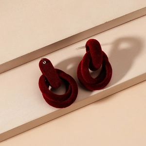 Close-up of interconnected geometric burgundy flocked earrings on a beige textured background