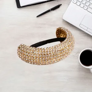 Golden wide curved rhinestone hair cuff with black elastic band on office desk background