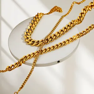 Golden stainless steel Cuban link anklet and slim chain displayed on white platform