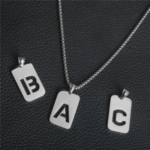 Detalle del colgante rectangular de acero plateado con letra calada y cadena fina