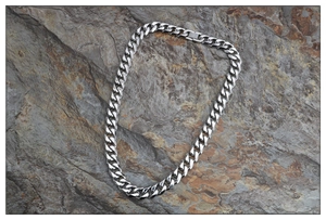 Detail of silver Cuban chain necklace with a box clasp on a rugged rock background
