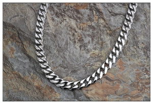 Polished silver stainless steel Cuban link necklace for men and women on a rock background