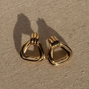 Minimalist gold titanium steel triangle stud earrings with textured ridges on beige fabric