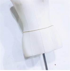 Detail of a minimalist gold metal body chain displayed on a white mannequin torso