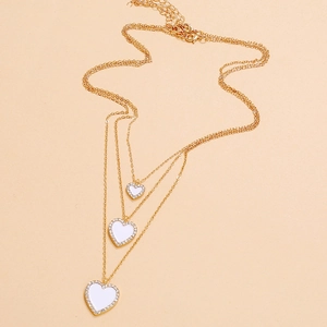 Three-layer gold necklace with white heart pendants and rhinestone borders on beige background