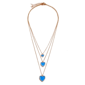 Close-up of triple-layered gold chain necklace featuring blue heart pendants and crystals