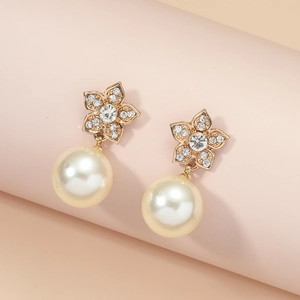 Elegant gold flower pearl earrings with crystals on a minimalist pink display stand