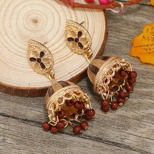 Ethnic χρυσά σκουλαρίκια jhumka με λουλούδι και κόκκινες χάντρες σε ξύλινο φόντο