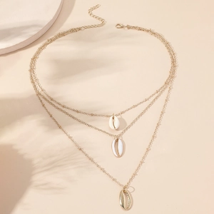 Collana a tre strati dorata con ciondoli a conchiglia naturali su sfondo beige estivo