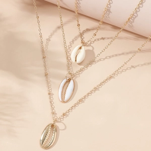 Collana dorata a tre strati con ciondoli a conchiglia naturale su sfondo beige caldo