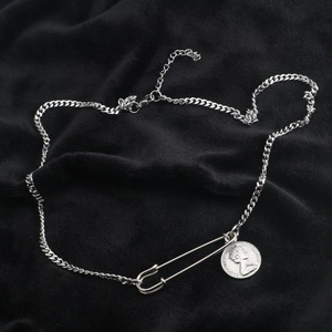 Macro detail of silver safety pin and Elizabeth II coin pendant on a Cuban chain
