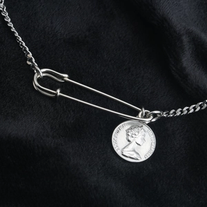 Titanium steel necklace with safety pin and coin pendant on black velvet background