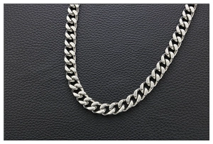 Detailed close-up of polished silver Cuban link chain over black leather background