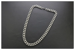 Macro detail of silver-colored thick cuban link chain on black leather background