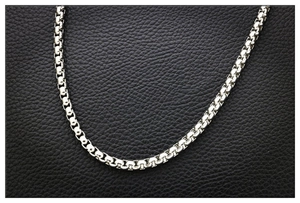 Close-up of a silver stainless steel box chain necklace on black leather background