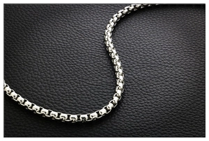 Close-up of a polished silver titanium steel box chain necklace on black leather