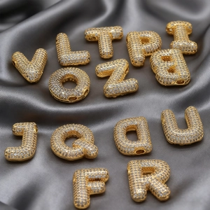Vista macro de colgantes de letras dorados con circonitas sobre fondo de seda