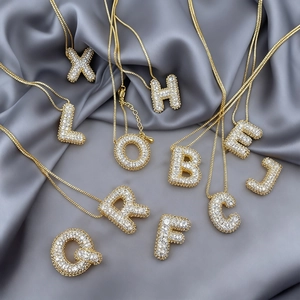 Vista de cerca de colgantes de letras burbuja bañados en oro con micro pavé de circonitas