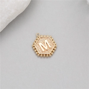 Macro detail of a 14K gold plated hexagonal M-letter pendant with beaded edges