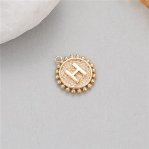 Macro shot of gold-plated 14K coin pendant featuring embossed letter H with beaded edge