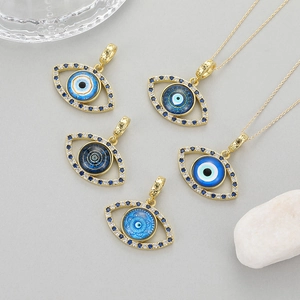 Böses-Auge-Anhänger mit blauen Zirkonia und Goldketten auf minimalistischer grauer Fläche