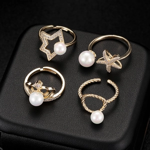 Detail of four gold-plated pearl rings with star, crown and starfish designs on black leather