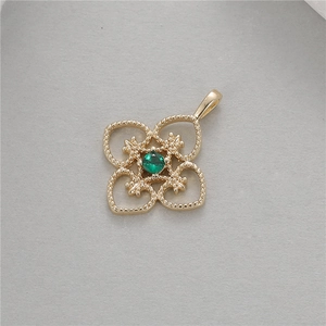 Close-up of vintage hollow gold pendant with green faceted gemstone and floral details