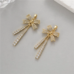 Detailed close-up of bow-shaped gold pendants with clear zircons and flowing tassels