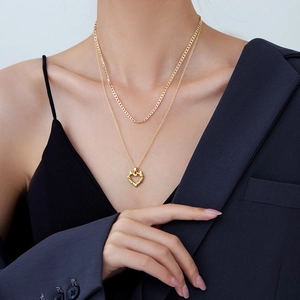 Gold double layer necklace featuring chunky curb chain and textured heart pendant on model