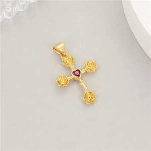 Macro shot of a 14K gold cross pendant with rose details and a red heart-shaped zircon