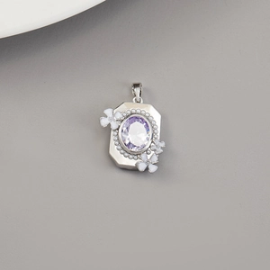 Dettaglio di un ciondolo vintage in argento con gemma viola e piccoli fiori in smalto bianco