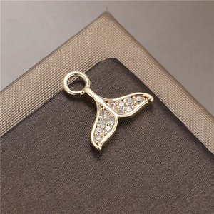 Detailed macro shot of a golden fish tail pendant with micro-paved zircons on a dark base