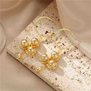 Elegante goldene Tropfenohrringe mit drei polierten Metallkugeln auf Natursteingrund