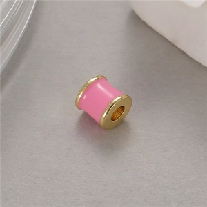 Detalle macro de una cuenta cilíndrica de esmalte rosa con bordes dorados para joyas DIY