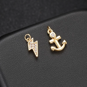 Detailed macro of 14K gold lightning and anchor pendants with zircons on black leather