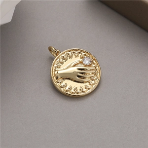Détail macro d'un pendentif pièce dorée avec une main tenant une pierre de zircon