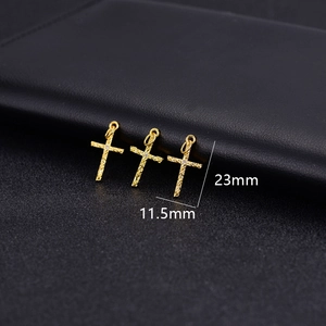 Macro detail of gold cross charms with hammered texture and tiny zircon inlay on black leather